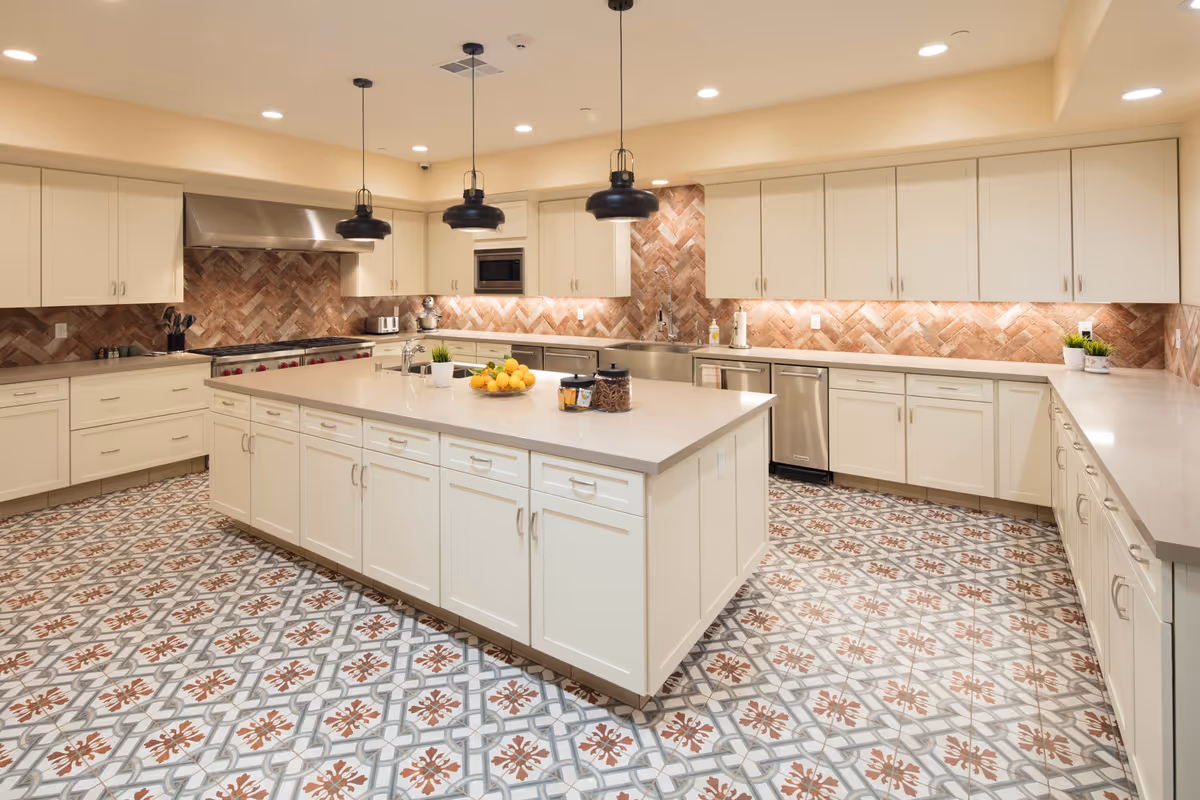 Spacious, well-lit kitchen with a large central island, cream cabinets, patterned tile floor, and pendant lighting.