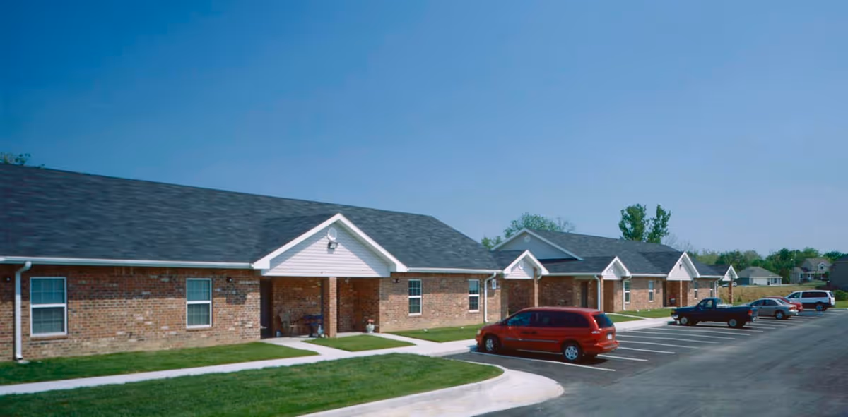 Exterior view of a single-story brick senior housing building with a parking lot.