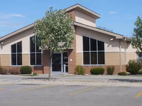 Genesis Senior Living Center exterior front with tall windows, trees, and shrubs.