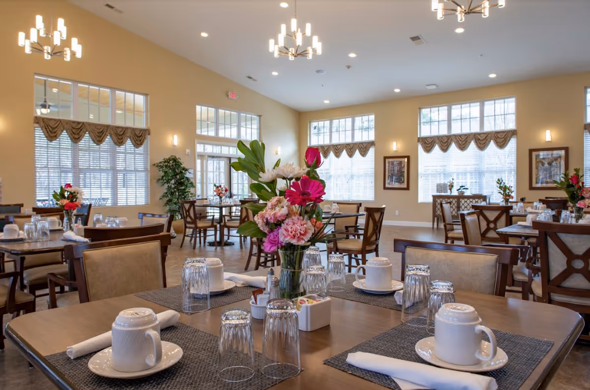 Bright, spacious dining room with tables set with cups, glasses, placemats and floral centerpieces.