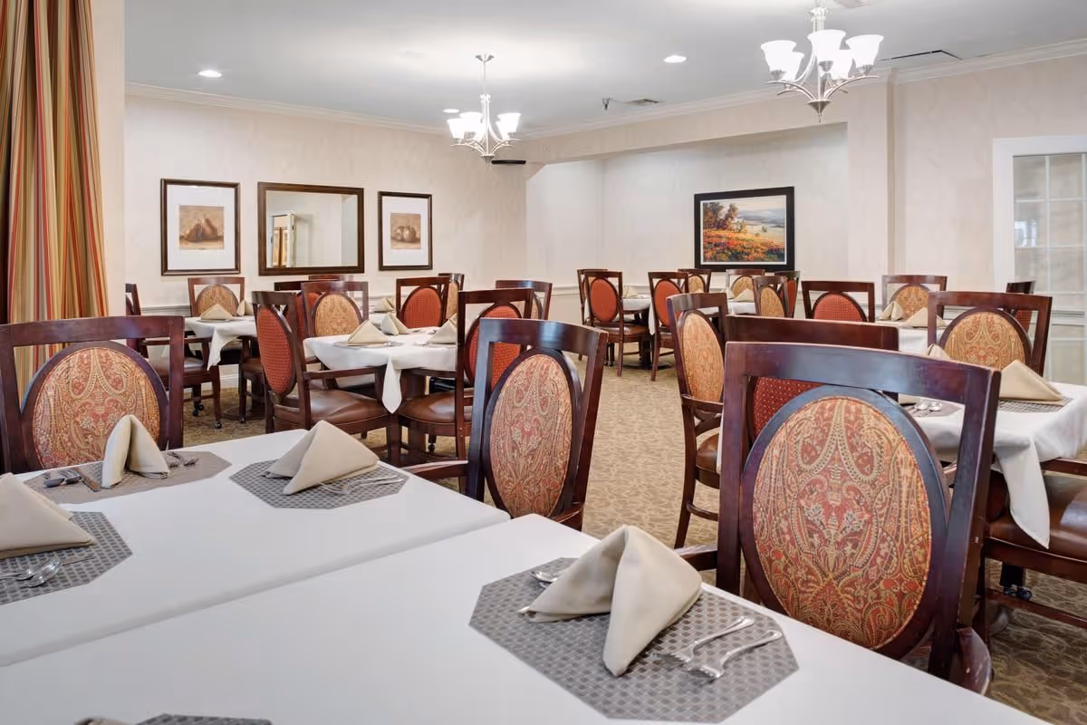 Formal dining room with multiple tables set with folded napkins and upholstered chairs.