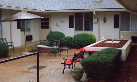 Outdoor courtyard at the facility with benches, hedges, and a shaded umbrella.