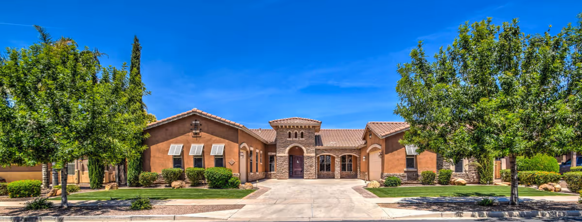 Front exterior view of Montelena Assisted Living and Memory Care facility with a single-story building featuring a tiled roof, stone and stucco facade, surrounded by green trees and shrubs under a clear blue sky.