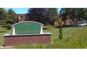 A brick-and-stone entrance sign for Westerly Rehabilitation & Healthcare Center on a grassy lawn with the facility buildings and trees behind it.