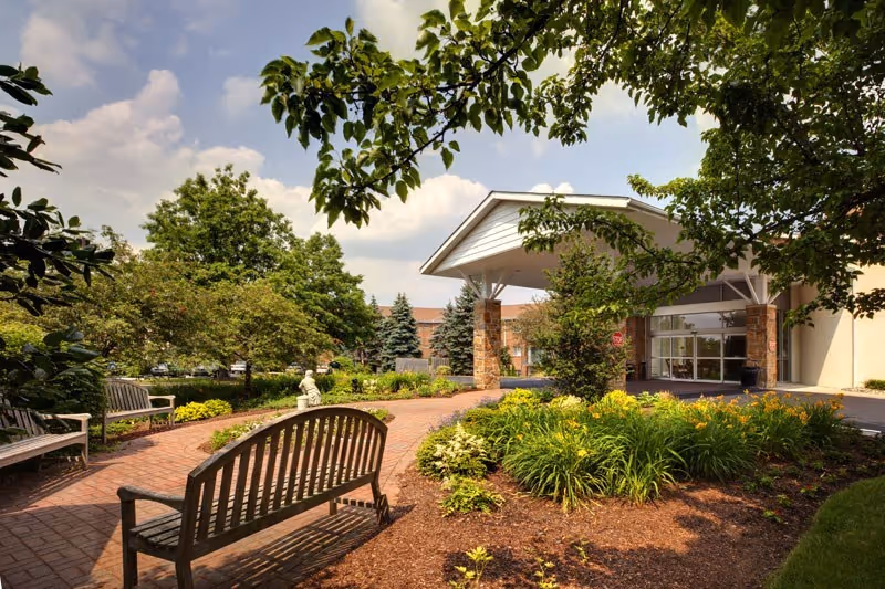 Landscaped front entrance of Normandy Farms Estates with benches, flowerbeds, and a covered porte-cochère.