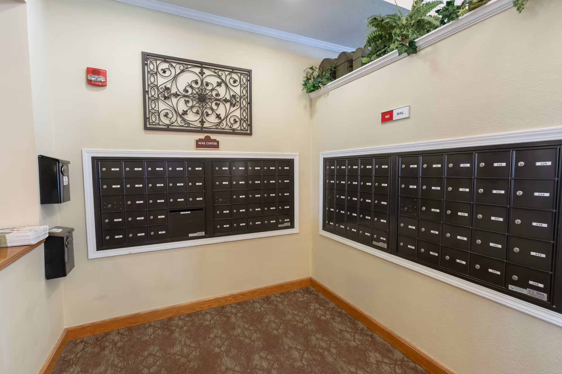 Interior mail center with rows of black apartment mailboxes mounted on two walls and decorative wall art above.