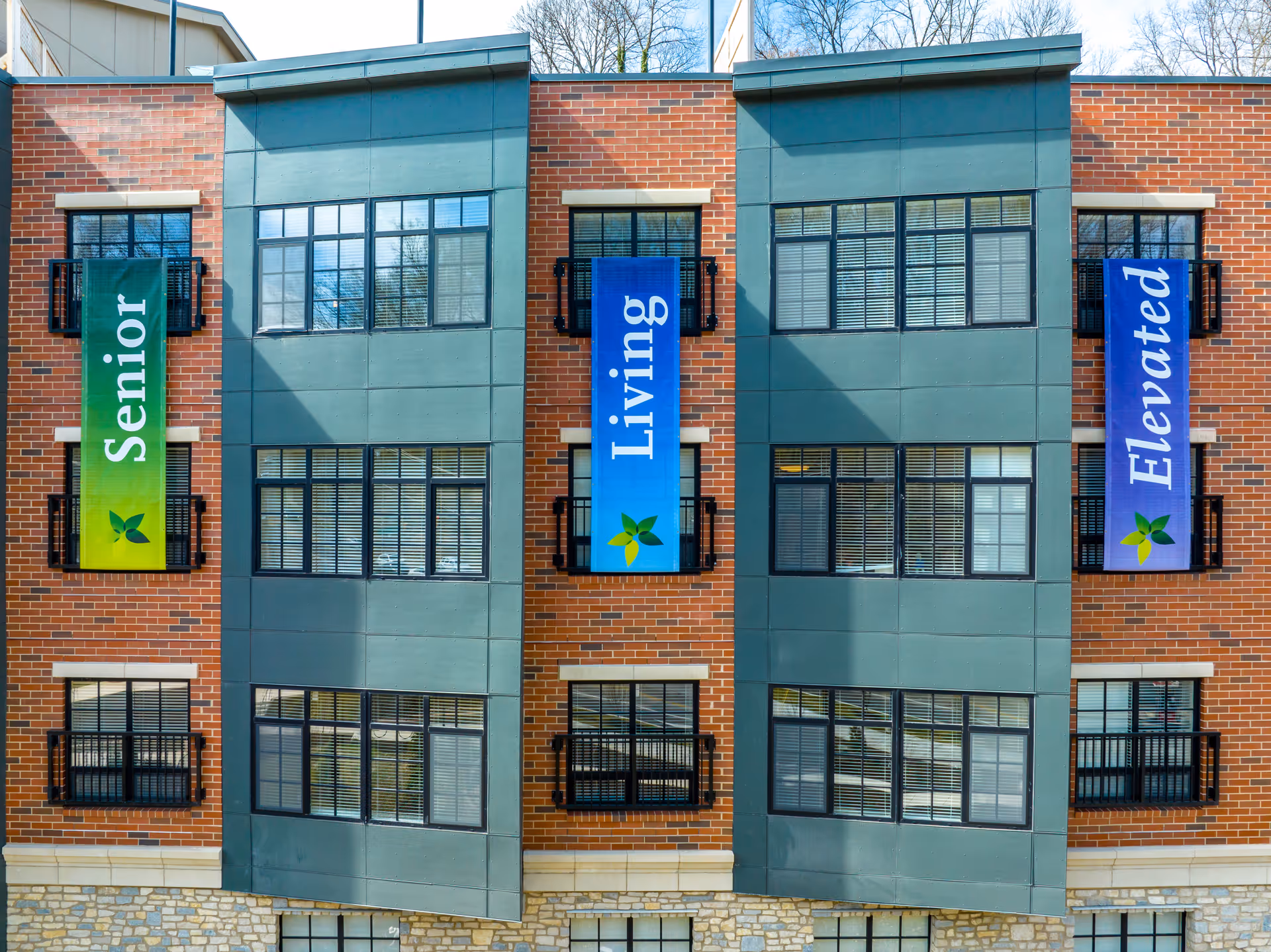 Front facade of a brick senior living building with three vertical banners reading 'Senior', 'Living', and 'Elevated'.