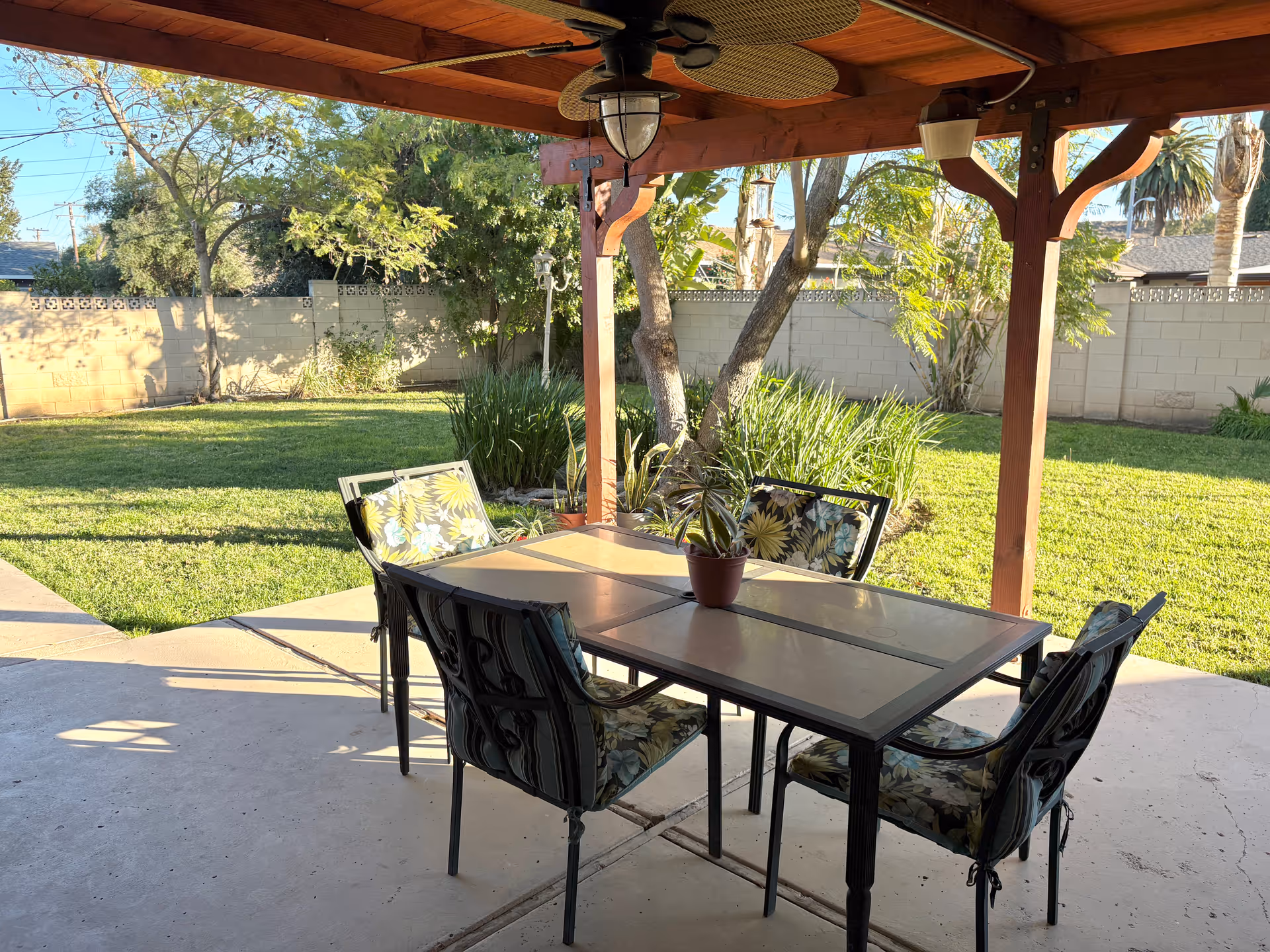 Covered backyard patio with a table and four chairs under a wooden pergola overlooking a grassy yard.