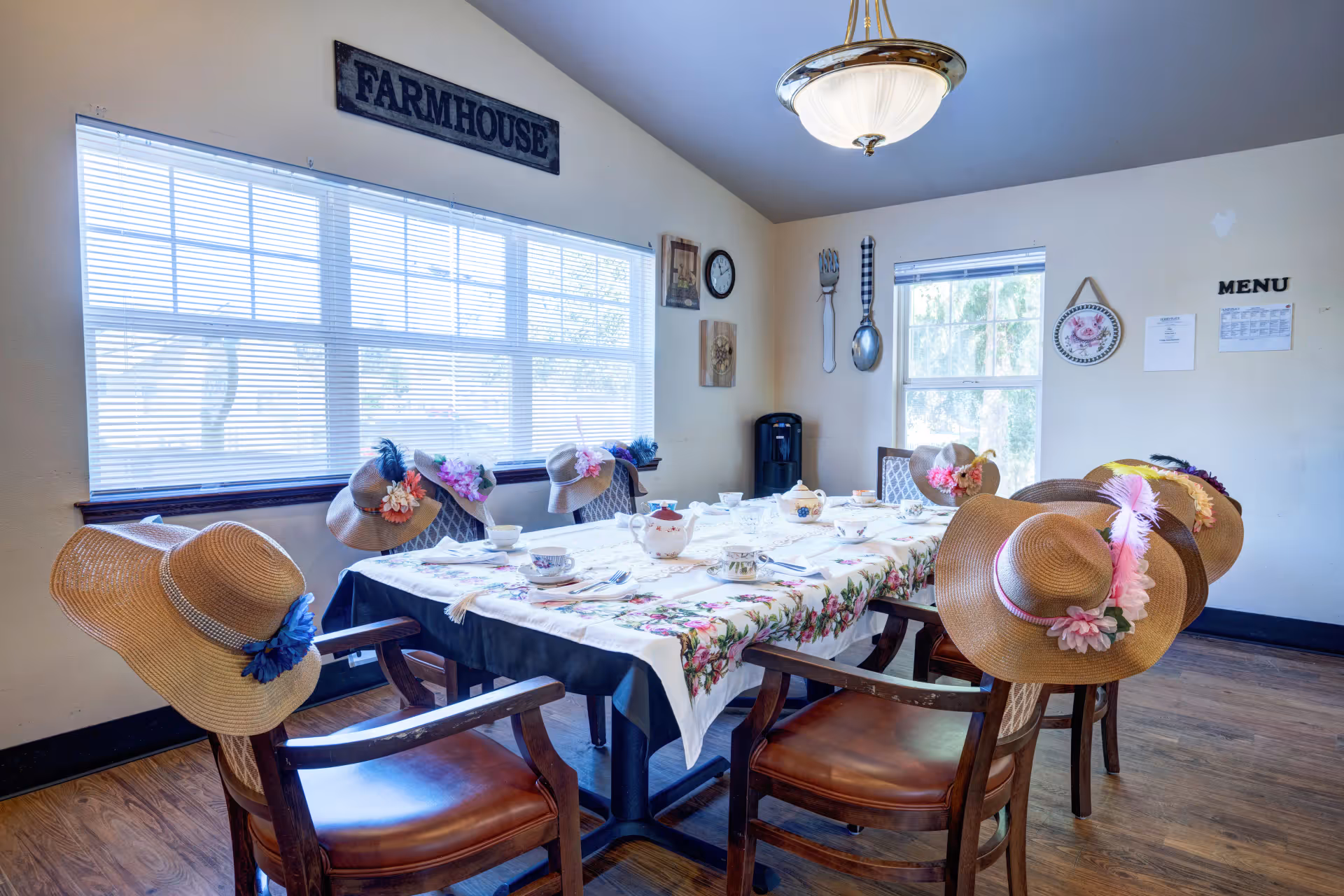 A sunlit dining room with a table set for tea and straw hats placed on the chairs under a 'Farmhouse' sign.