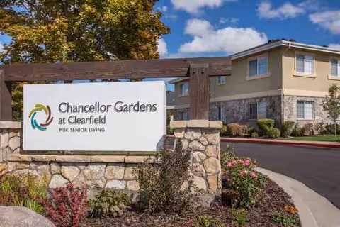 Exterior view of Chancellor Gardens senior living facility with sign and landscaped entrance.