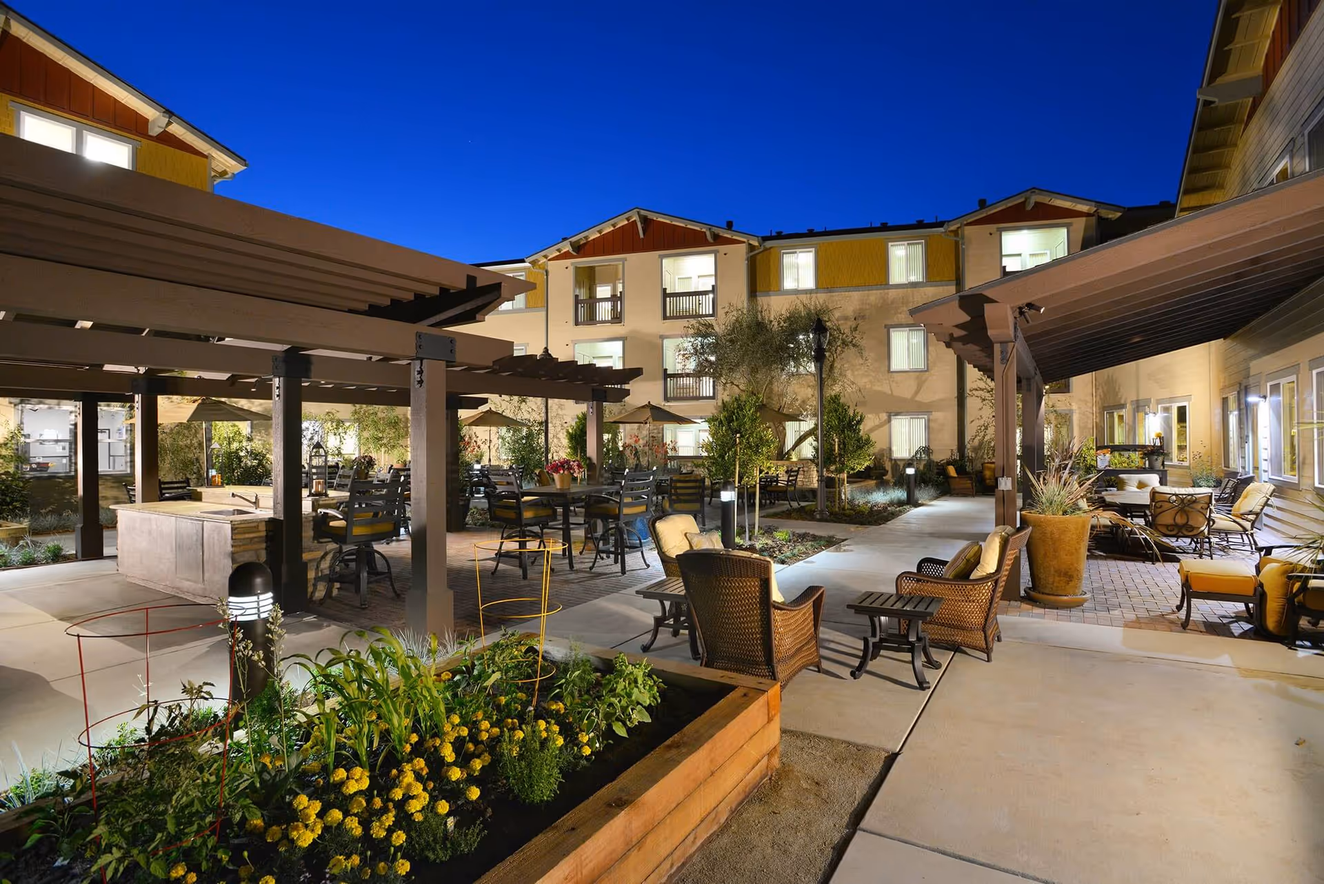 Nighttime exterior view of a senior living courtyard with seating under pergolas and surrounding buildings.