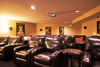 Dimly lit media room with rows of leather recliner chairs facing a ceiling-mounted projector.