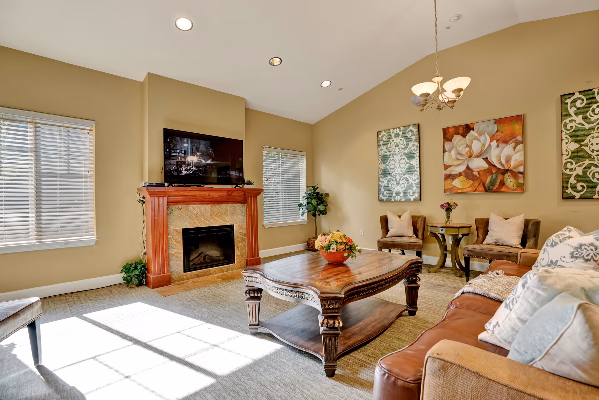 Bright living room with a fireplace and wall-mounted TV, a wooden coffee table, sofa and accent chairs beneath decorative artwork.