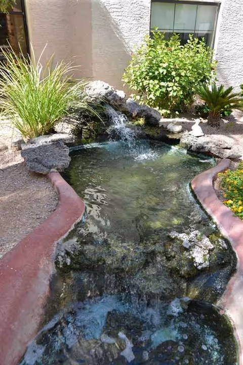 A narrow outdoor water feature runs along rocks beside a building.
