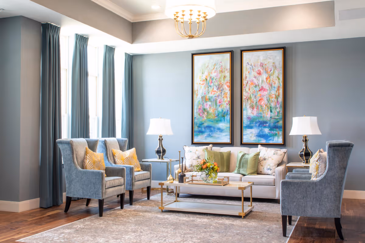 Bright, elegant lounge with a sofa, armchairs, coffee table, lamps, and colorful framed artwork on the wall.