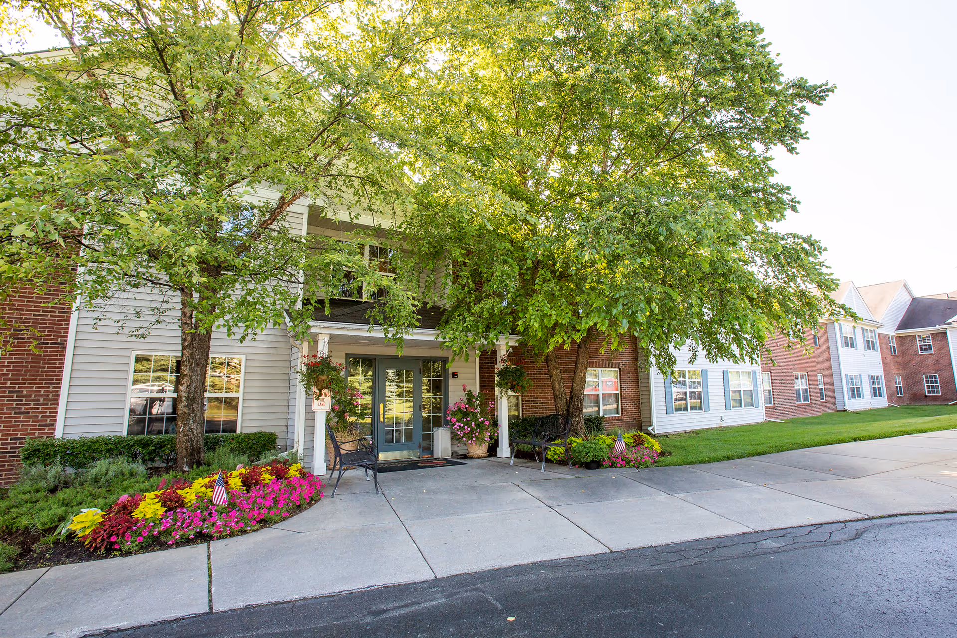 Exterior view of Independence Village of White Lake featuring greenery and colorful flowers.