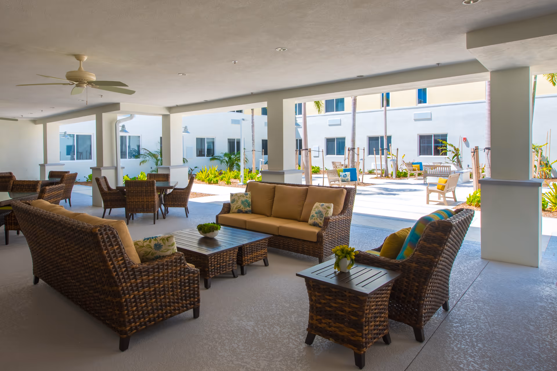 Covered outdoor seating area with wicker sofas, chairs, and tables opening onto a sunny courtyard.