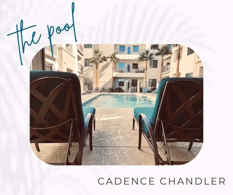 View of an outdoor swimming pool with two empty lounge chairs facing the pool, surrounded by a multi-story building with balconies and palm trees.