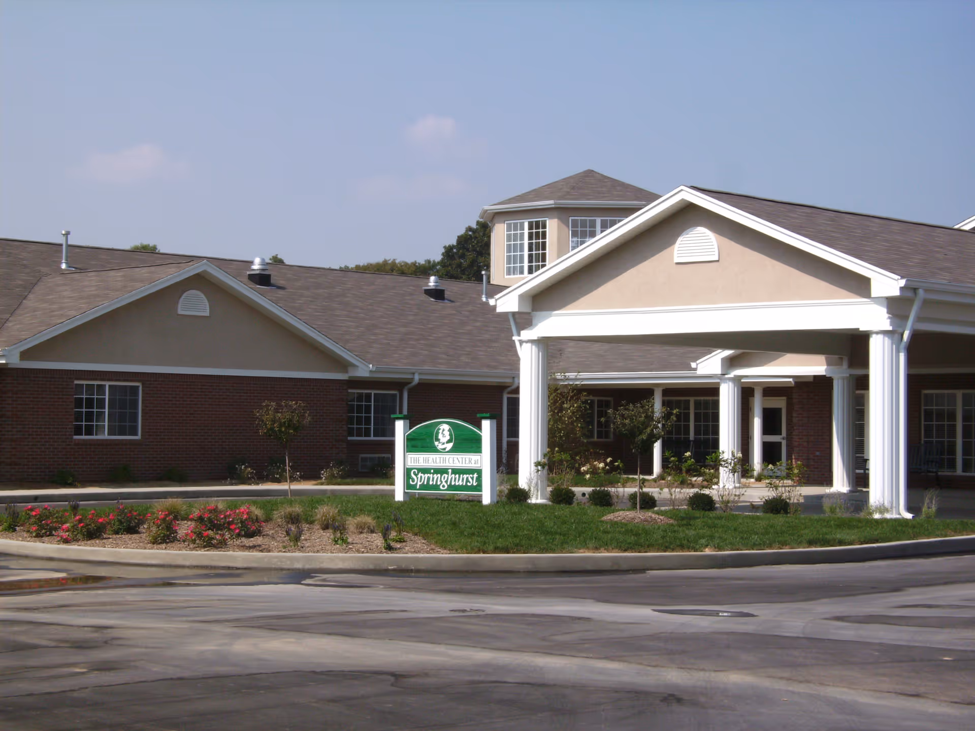 Exterior view of Springhurst Health Campus building with a covered entrance supported by white columns, landscaped greenery, and a sign in front that reads 'The Health Center at Springhurst'.