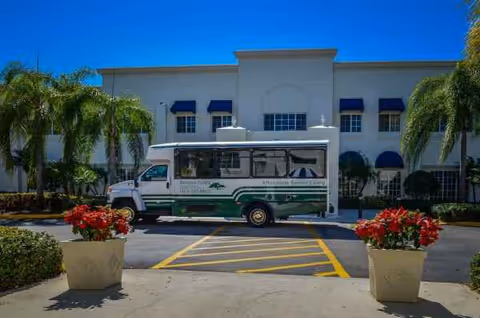 Front view of Banyan Place senior living facility with a shuttle bus and palm trees.