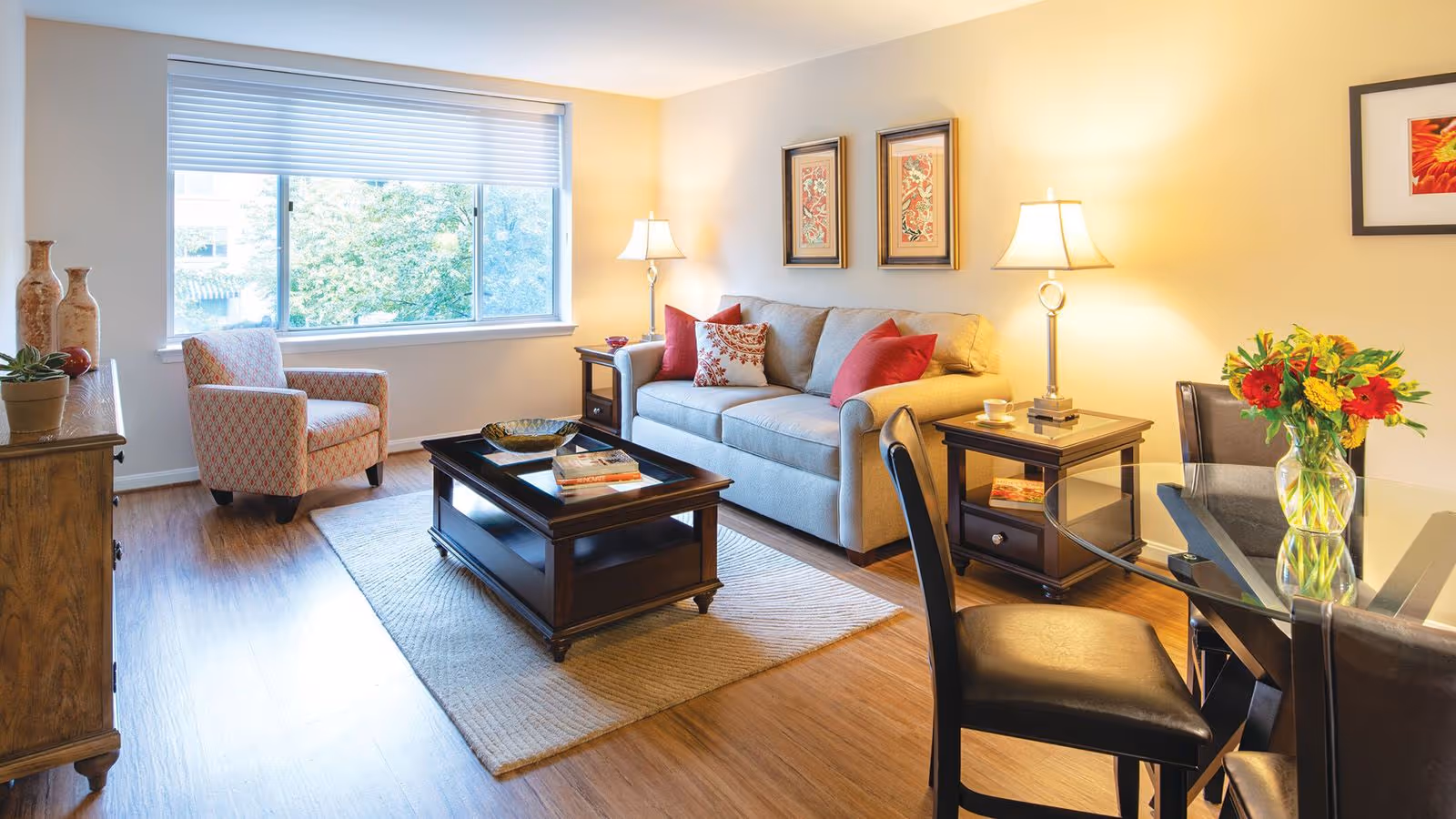 Bright furnished living room with a sofa, armchair, coffee table, dining table and chairs, and a large window.