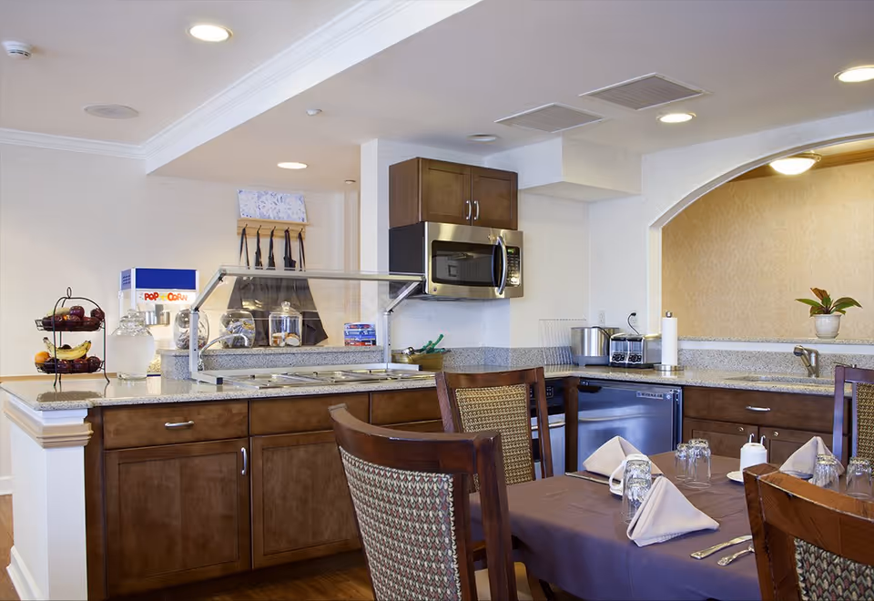 Communal dining area with a buffet counter, microwave and cabinets, and a table set with napkins and glassware.