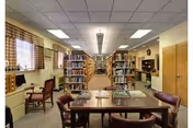 Interior library/reading room with bookshelves down the center aisle and a table with chairs in the foreground.