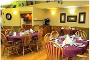 Dining room with round tables, purple tablecloths, and wooden chairs.