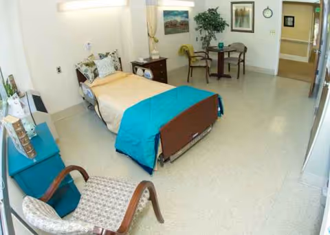 A hospital-style senior facility bedroom with a bed, chairs, and a small table.