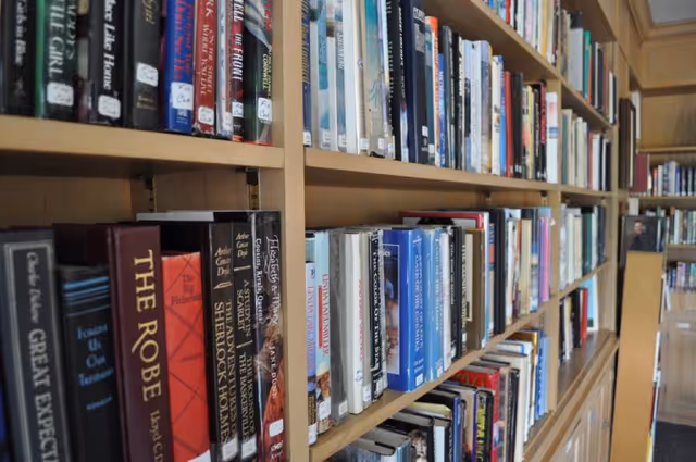 Bookshelves filled with a variety of books in a well-lit room, likely a library or reading area within the facility.