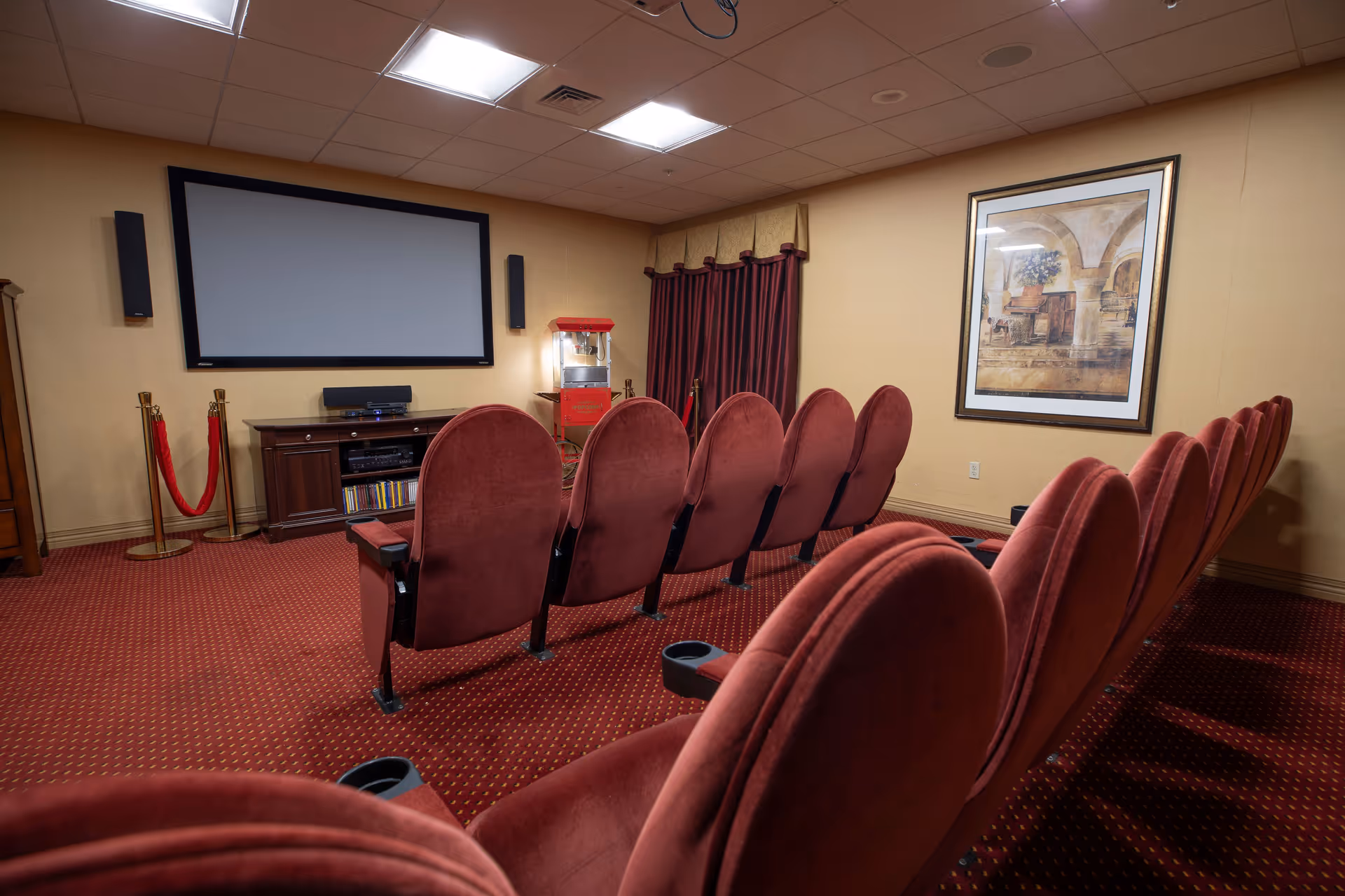 Private screening room with rows of red upholstered theater seats facing a large projection screen and a popcorn machine.