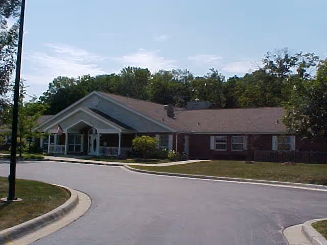 Single-story brick building with a gabled roof and a covered entrance, surrounded by trees and a curved driveway in front.