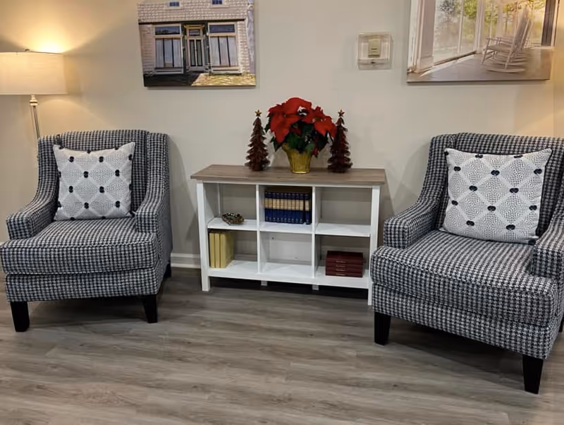 Two patterned armchairs flank a small white shelving unit topped with a poinsettia and holiday decorations in a cozy seating area.