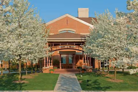Front entrance of a brick senior living building framed by blossoming trees.