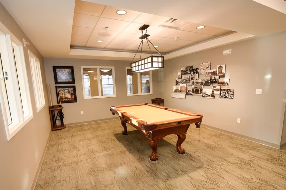Interior recreation room with a pool table centered under a hanging light and a photo collage on the wall.