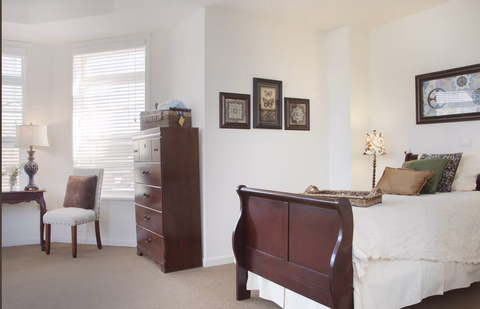 Bright furnished bedroom with a wooden sleigh bed, chest of drawers, chair, and framed wall art.