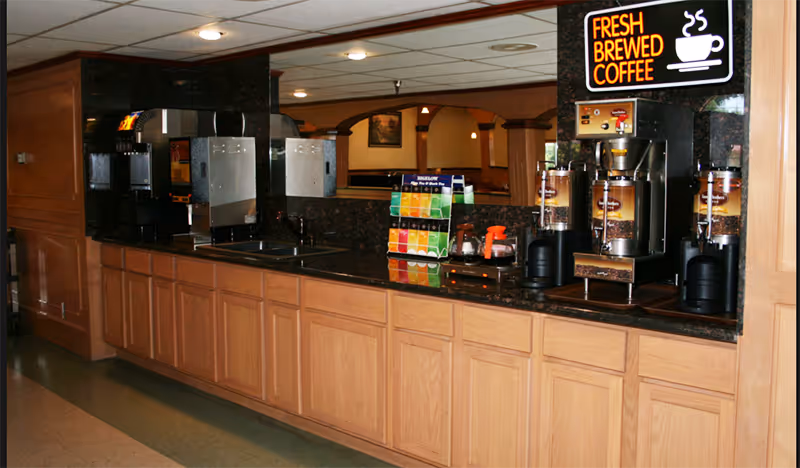 Countertop beverage station with coffee dispensers, a tea display, and a 'Fresh Brewed Coffee' sign in an interior dining area.