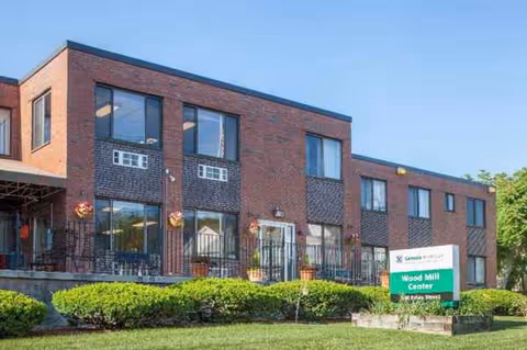 Two-story brick senior care building with large windows and a manicured lawn.