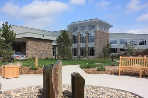 Exterior view of PioneerCare Center with stone facade, benches, and landscaped courtyard.
