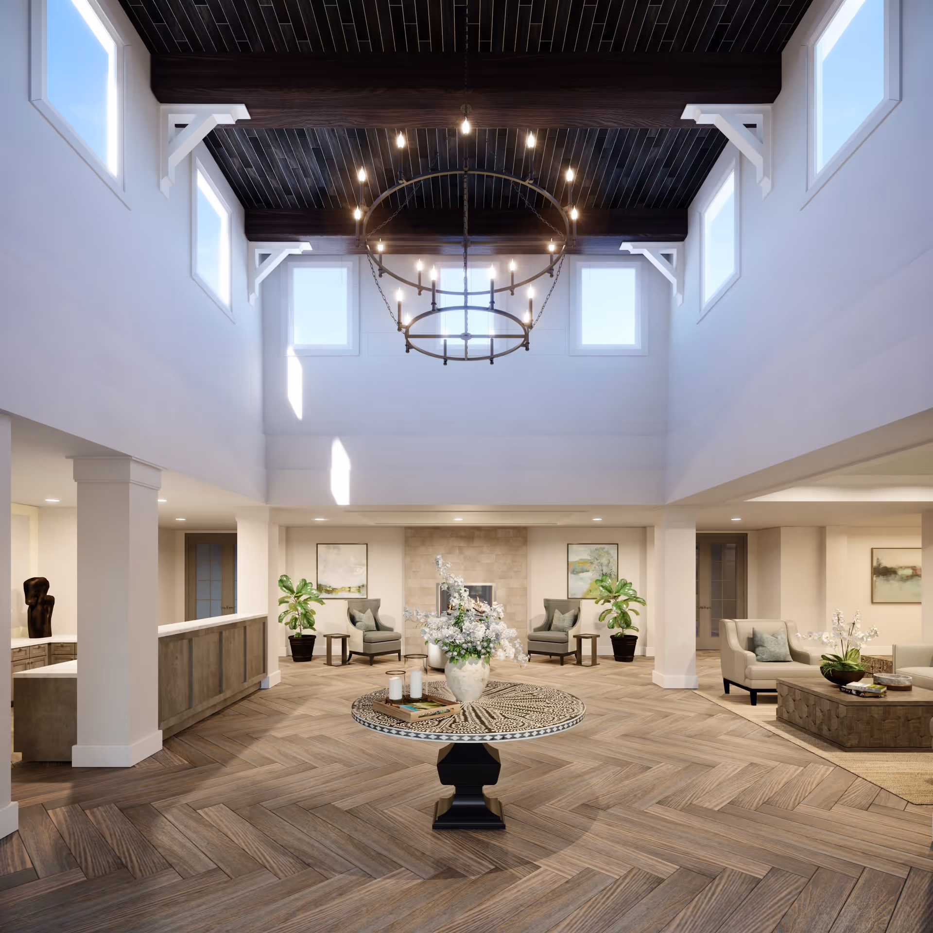 Spacious and elegant senior living facility common area with high ceilings, large windows, a circular chandelier, a decorative round table with a flower arrangement in the center, comfortable seating areas with armchairs and side tables, potted plants, and framed artwork on the walls.