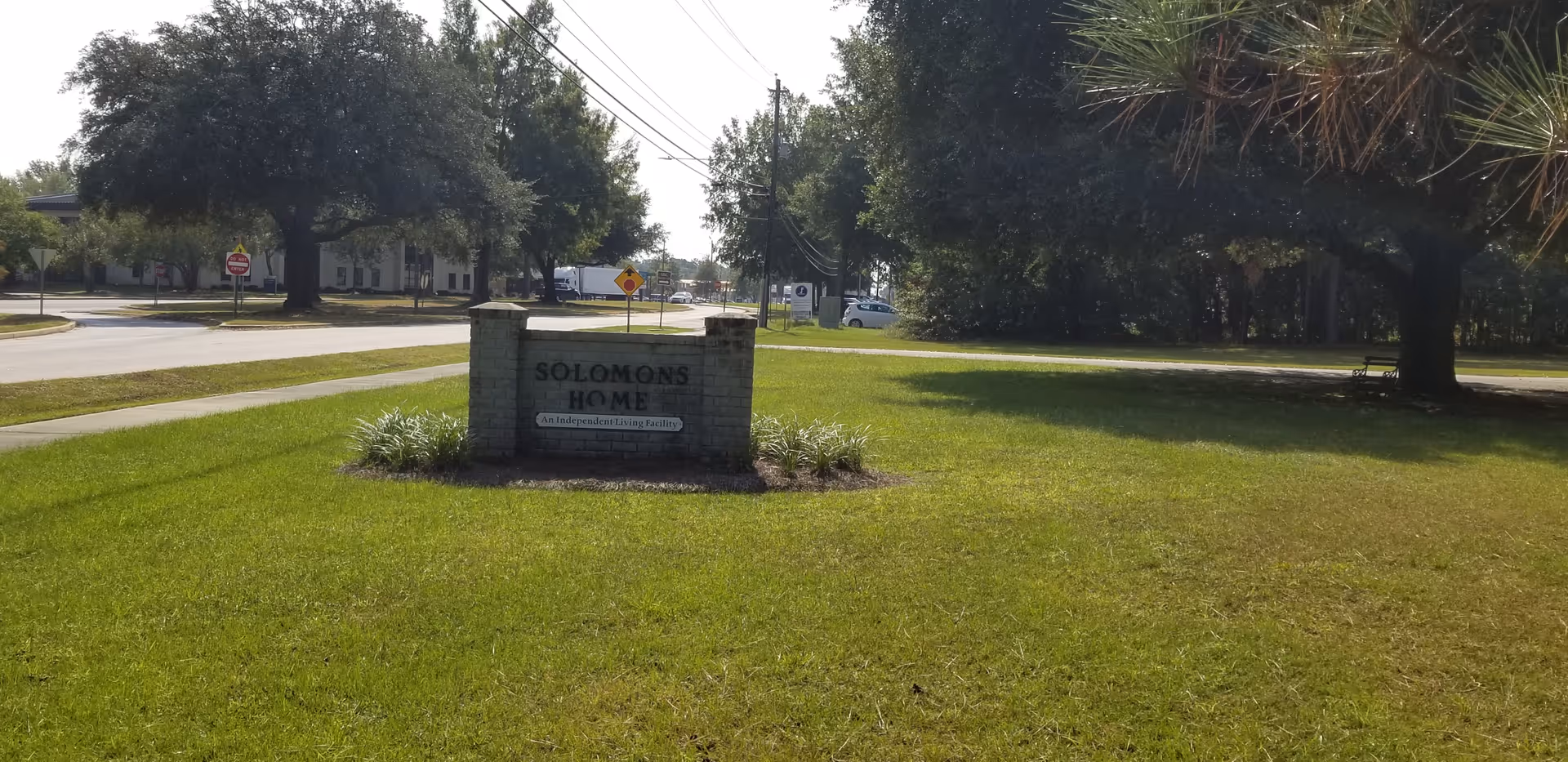 A brick sign reading "Solomons Home" sits on a grassy lawn with trees and a street in the background.