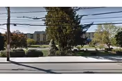 Street view of St. Cabrini Nursing Home showing a multi-story building partially obscured by large trees and shrubs, with a sidewalk and power lines in the foreground.