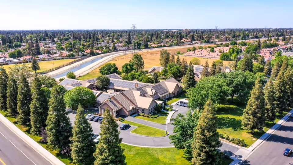 Aerial view of Riverstone Terrace Senior Living buildings surrounded by trees, lawns, parking areas, and nearby neighborhood.