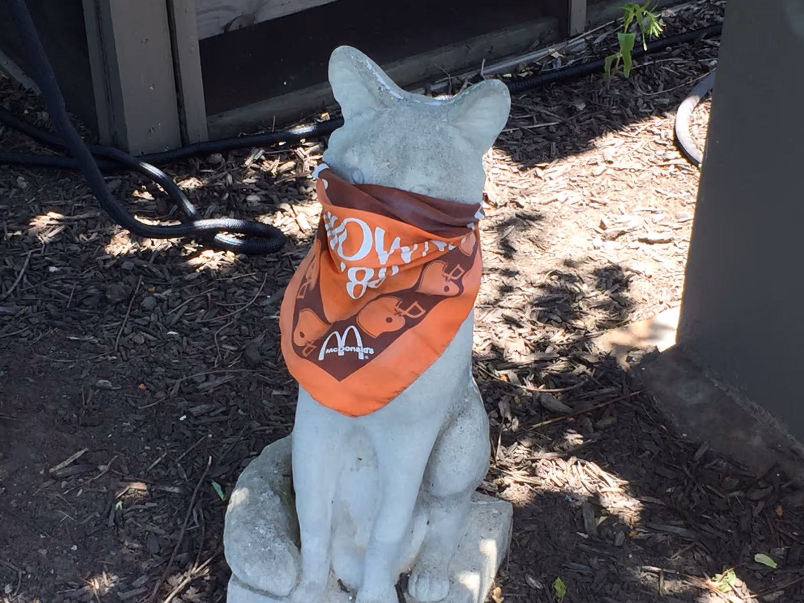A stone cat statue outdoors wearing an orange bandana.