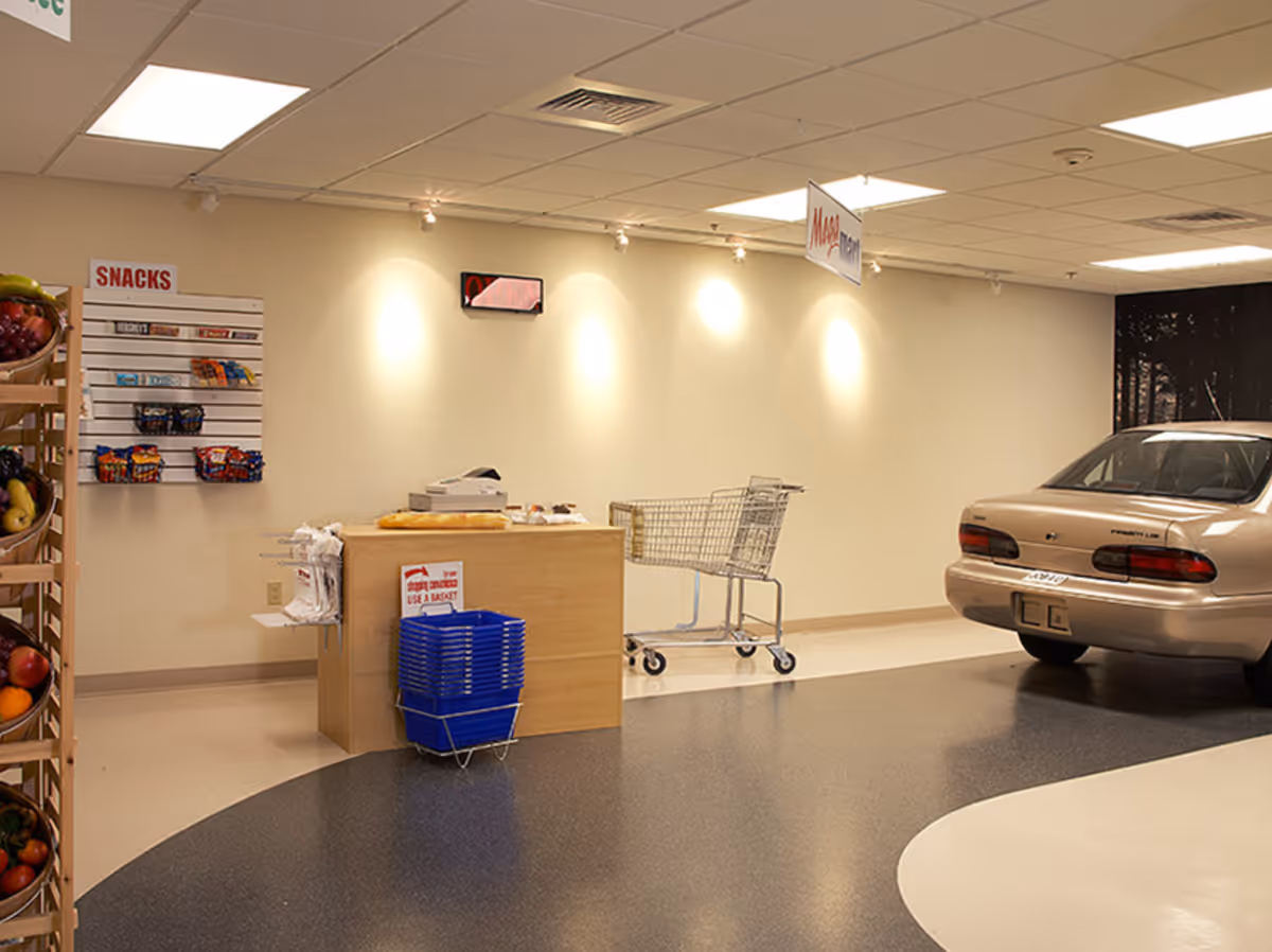 Small indoor market area with a checkout counter, snack displays, shopping carts, and a parked car.