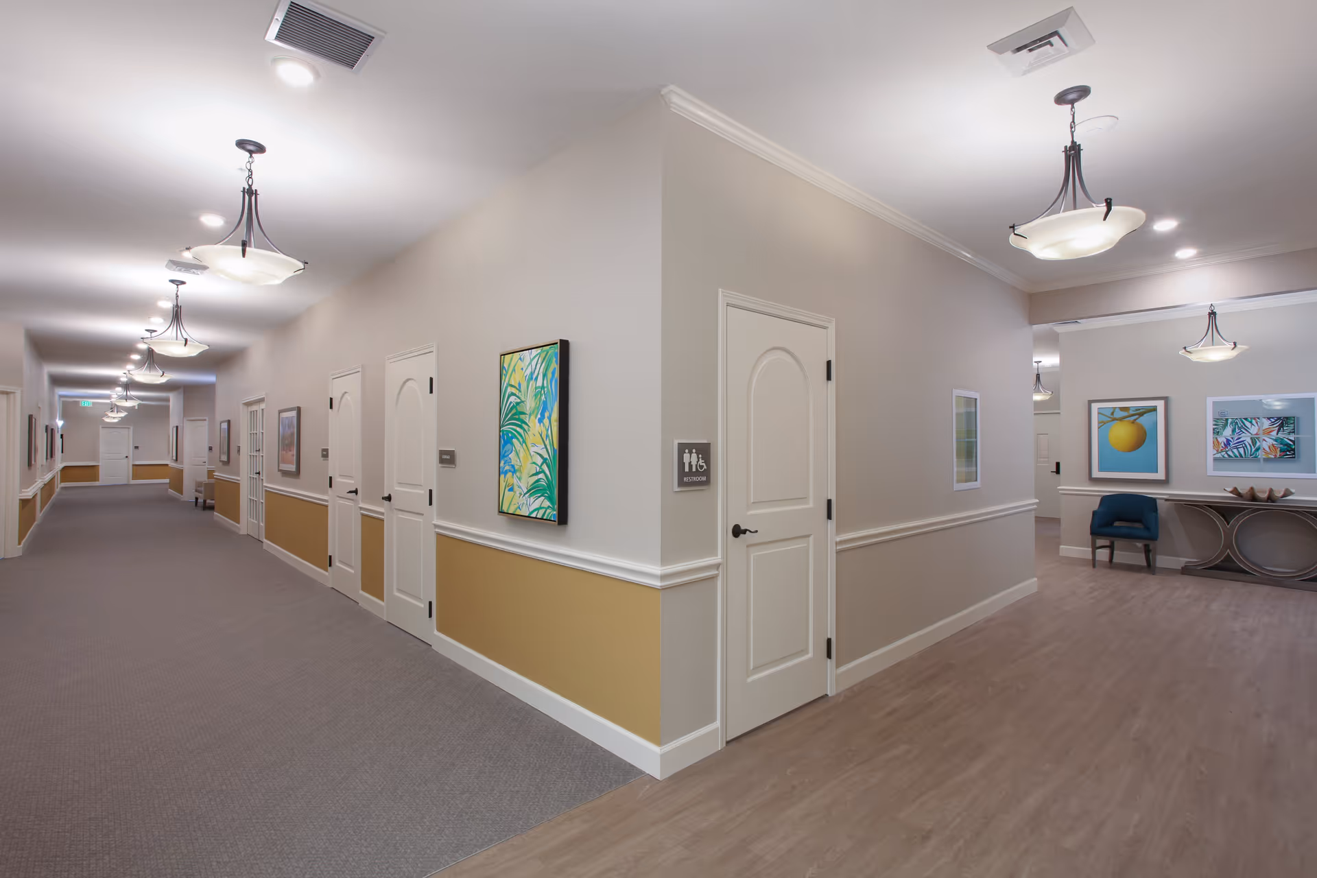 Well-lit interior hallway and common area with doors, artwork, seating, and pendant lights.