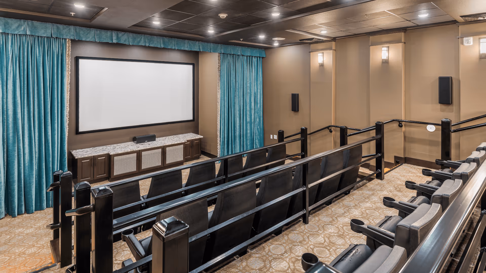 Small community movie theater with rows of reclining seats facing a large projection screen framed by teal curtains.