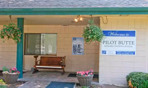 The facility entrance shows a welcome sign, bench, hanging baskets, and potted flowers.