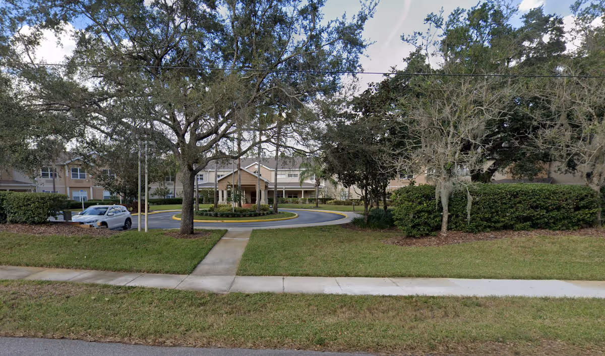 Front exterior view of Chapman Manor at Lutz showing a circular driveway with a covered entrance, surrounded by trees, bushes, and a well-maintained lawn.