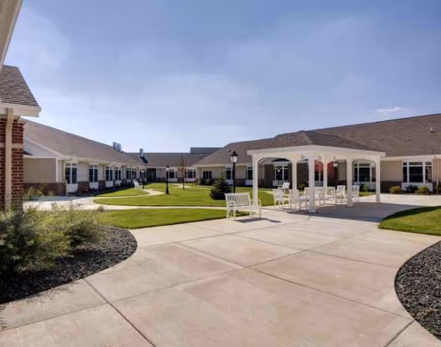 Wide outdoor courtyard of a senior facility with paved paths and white seating.